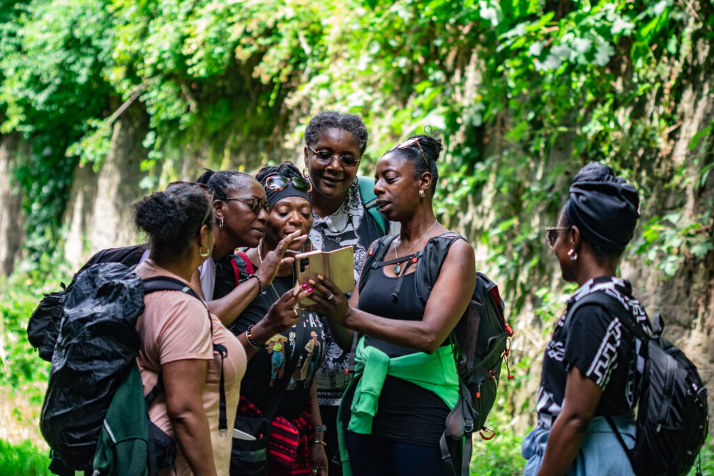 Group of women from Bristol Steppin Sisters gathered on a leafy path, looking at a phone together during a walk