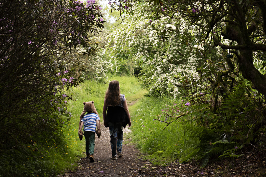 Two young children walking along a woodland path surrounded by greenery.