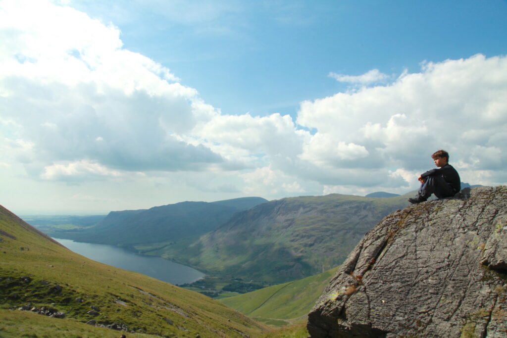 Child sitting on a rocky outcrop overlooking a lake and hills