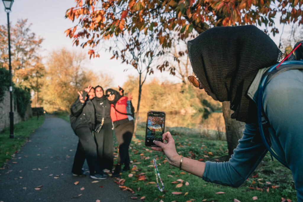 Person taking a photo of three people posing together on a park path