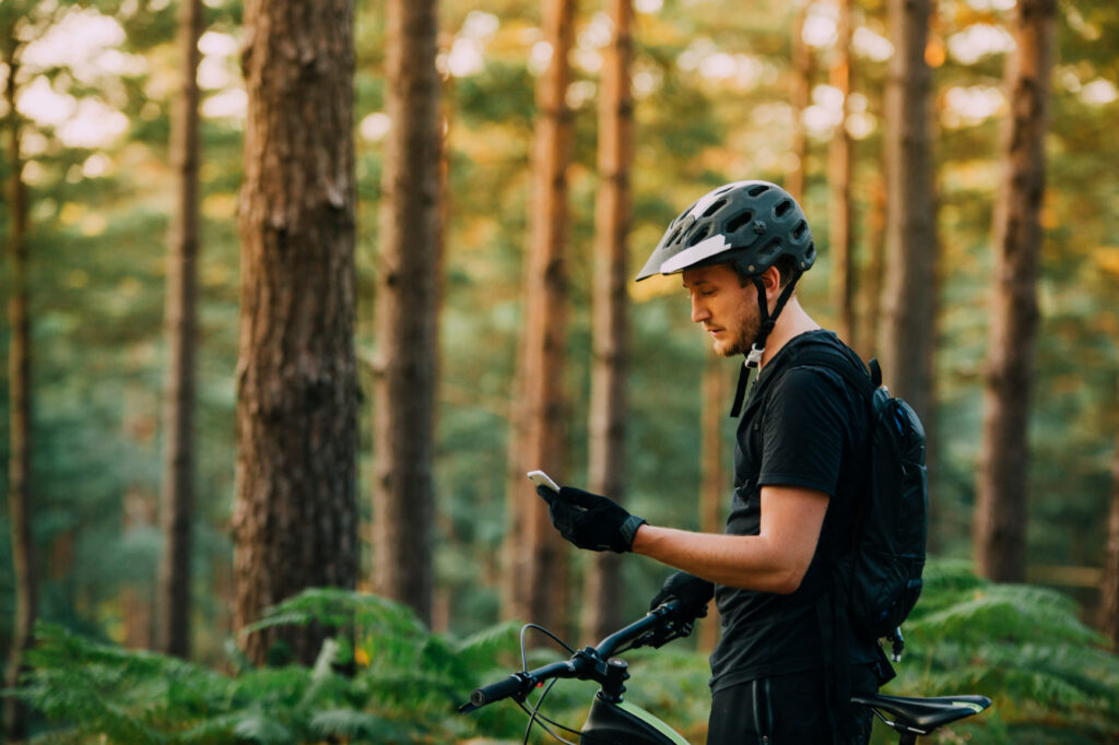 Man with a bicycle checking his phone on a forest trail