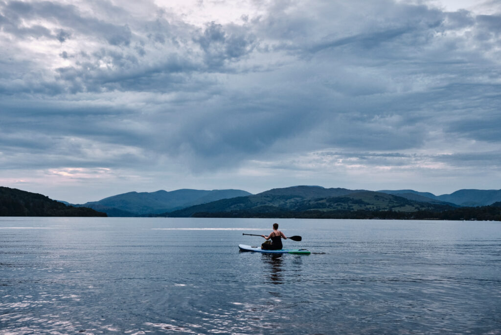 Person paddleboarding alone on a calm lake with hills in the distance.