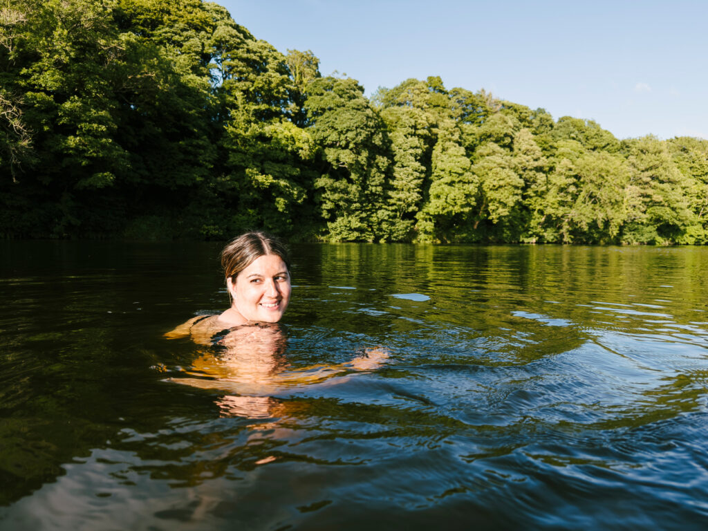 Woman swimming in a river with trees along its bank.