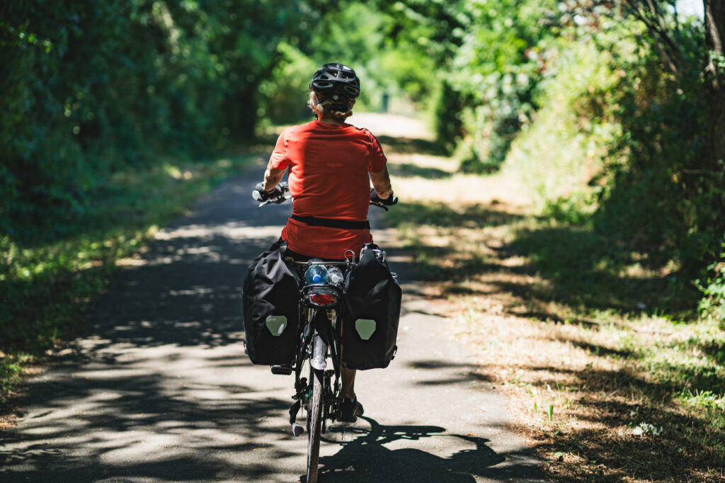 Woman cycling along a shaded path surrounded by greenery.