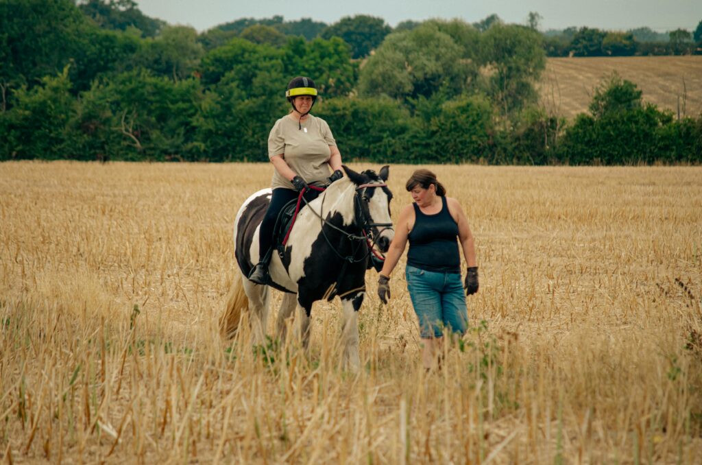 Person riding a horse led by another person through a field.