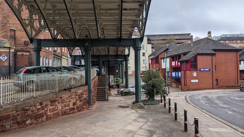 Some steps going up between two roads under the Iron Bridge, with buildings either side.